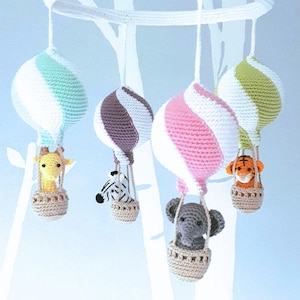 Op de afbeelding: Een witte gehaakte mobiel met vijf hangende elementen. Vier van de elementen zijn gehaakte luchtballonnen in roze, groen, blauw en bruin. Aan elke ballon hangt een gehaakt dier: een giraffe, een zebra, een olifant en een tijger.