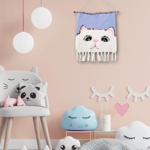 May include: A light pink wall with a white cat face woven wall hanging, a gray chair with cat ears, a panda pillow, and a blue cloud-shaped nightlight.