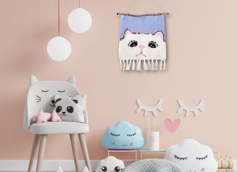 May include: A light pink wall with a white cat face woven wall hanging, a gray chair with cat ears, a panda pillow, and a blue cloud-shaped nightlight.