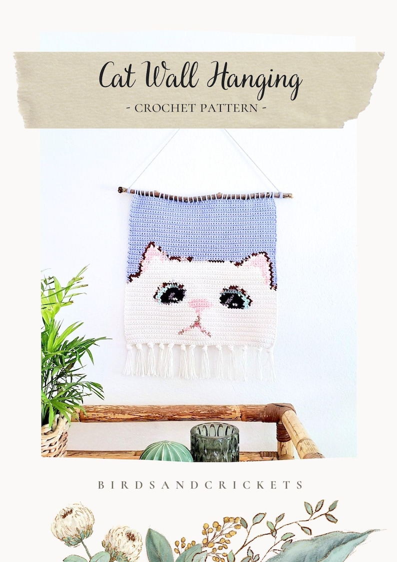 May include: Crochet cat wall hanging with a light blue and white color scheme. The cat has black eyes and a pink nose. The hanging is attached to a wooden stick with a white string. The text "Cat Wall Hanging - CROCHET PATTERN -" is at the top of the image. The text "BIRDSANDCRICKETS" is at the bottom of the image.