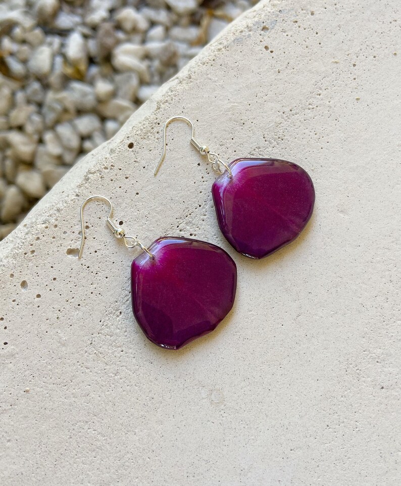 May include: A pair of dangle earrings with a deep purple resin petal shape. The earrings have silver hooks.