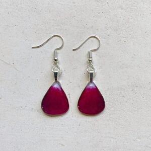 May include: A pair of dangle earrings with teardrop-shaped purple resin pendants and silver hooks.