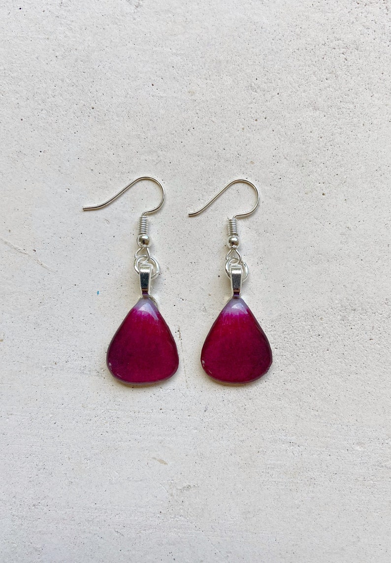 May include: A pair of dangle earrings with teardrop-shaped purple resin pendants and silver hooks.