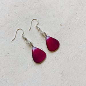 May include: A pair of dangle earrings with silver hooks and teardrop-shaped resin pendants in a deep burgundy color.