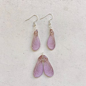 May include: A set of earrings and a pendant featuring delicate, translucent purple maple seed pods. The jewelry is made with real maple seeds encased in resin.