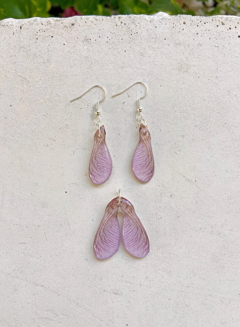 May include: A set of earrings and a pendant featuring delicate, translucent purple maple seed pods. The jewelry is made with real maple seeds encased in resin.