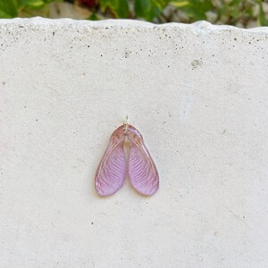 Puede incluir: Un par de pendientes de semillas de arce rosa con un bucle de alambre dorado.