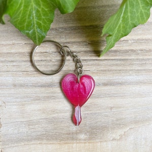 May include: A pink heart-shaped keychain with a white swirl design. The keychain is attached to a silver key ring.