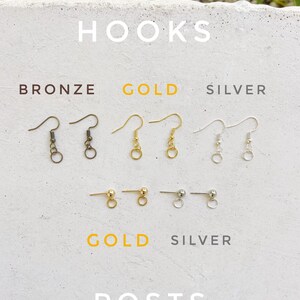 May include: A close-up of earring hooks and posts in bronze, gold, and silver. The hooks are shown in three different finishes: bronze, gold, and silver. The posts are shown in gold and silver.