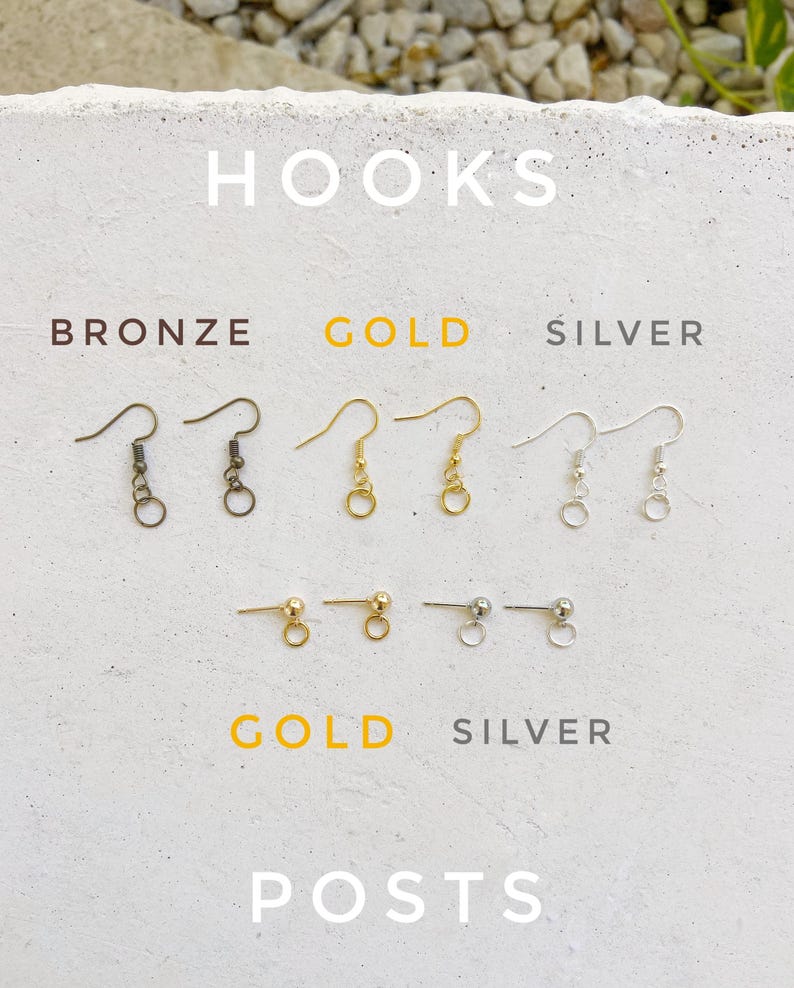 May include: A close-up of earring hooks and posts in bronze, gold, and silver. The hooks are shown in three different finishes: bronze, gold, and silver. The posts are shown in gold and silver.