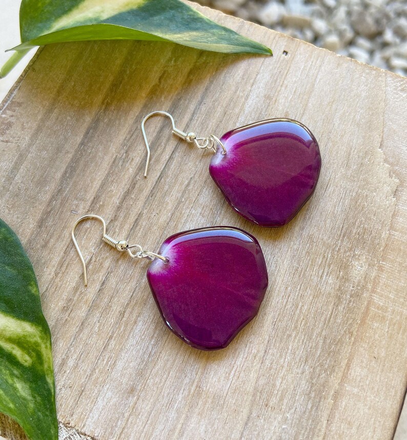 May include: A pair of earrings featuring a purple resin petal design. The earrings are made with silver hooks.