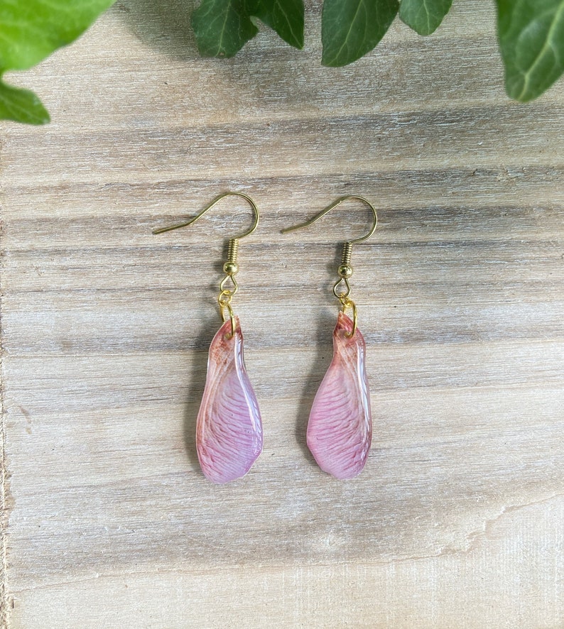 May include: A pair of delicate earrings featuring pink and white resin flower petals with gold hooks.