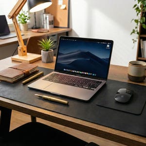 Matte black full grain leather desk mat, executive desk pad styling, laptop, stacked notebooks, plant