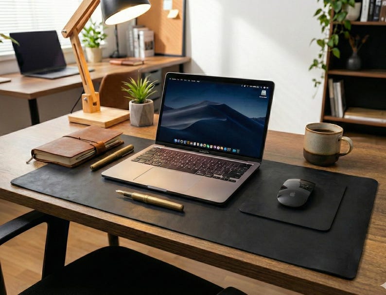 Matte black full grain leather desk mat, executive desk pad styling, laptop, stacked notebooks, plant