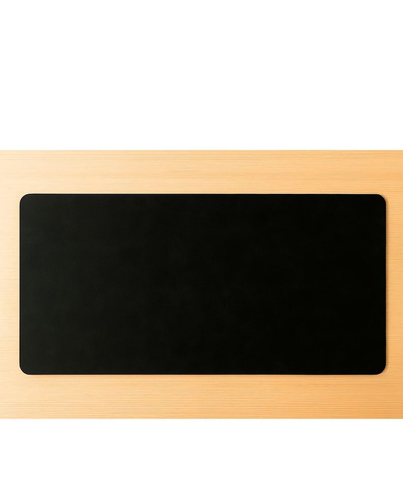 Flat black full grain leather desk mat, clean rectangular leather desk pad on light wood surface
