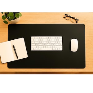 Minimal black full grain leather desk mat used as large leather mouse pad, keyboard and notebook arranged