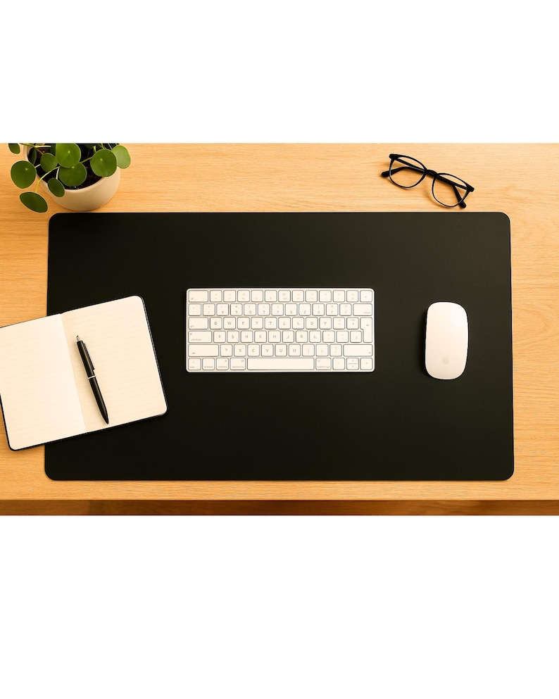 Minimal black full grain leather desk mat used as large leather mouse pad, keyboard and notebook arranged