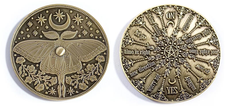 Puede incluir: Una moneda de lat&oacute;n con un dise&ntilde;o de polilla y flores en un lado y un dise&ntilde;o circular con las palabras "divine timing", "let go", "time is right", "new direction", "worry not", "yes", "on", "reconsider", "not right time", "right direction", "unlikely", "moil diy" en el otro lado.