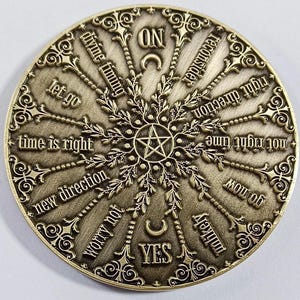 May include: A circular, brass-colored divination tool with a pentagram in the center and a compass-like design with phrases like "let go", "time is right", "new direction", "worry not", "yes", "no", "reconsider", "right direction", "not right time", "my ob", "unlikely", "divine timing", and "on".