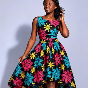May include: A sleeveless high-low dress featuring a black base with a repeating floral pattern in vibrant shades of magenta, turquoise, and yellow. The dress has a fitted bodice, a defined waistline, and a voluminous skirt that is shorter in the front.
