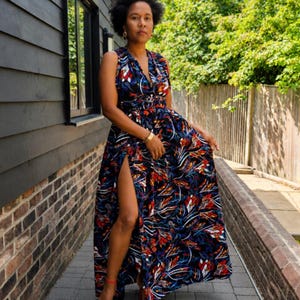 May include: A sleeveless floor-length maxi dress featuring a deep V-neckline, a fitted waist, and a high side slit. The fabric displays a vibrant, multi-colored abstract pattern with prominent shades of blue, red, white, and black throughout.
