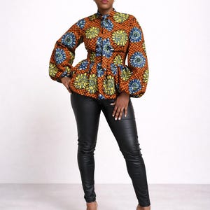 May include: An orange, yellow, and blue floral print top with long, puffy sleeves and a peplum waist. The top is paired with black leather pants and black high-heeled sandals. The outfit is set against a white background.