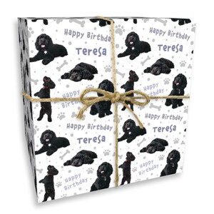 May include: Wrapped gift with a white background featuring a pattern of black dogs, paw prints, and bones. The words "Happy Birthday Teresa" are repeated throughout the design. The gift is tied with twine.