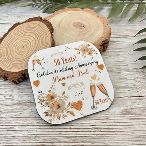 A 50th anniversary coaster with a floral design and champagne glasses, celebrating the golden wedding anniversary of a mother and father.
