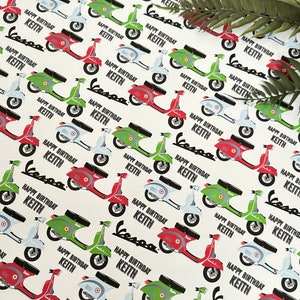 May include: White wrapping paper with a repeating pattern of colorful Vespa scooters. The scooters are red, green, and blue. The text "Happy Birthday Keith" is repeated throughout the pattern.