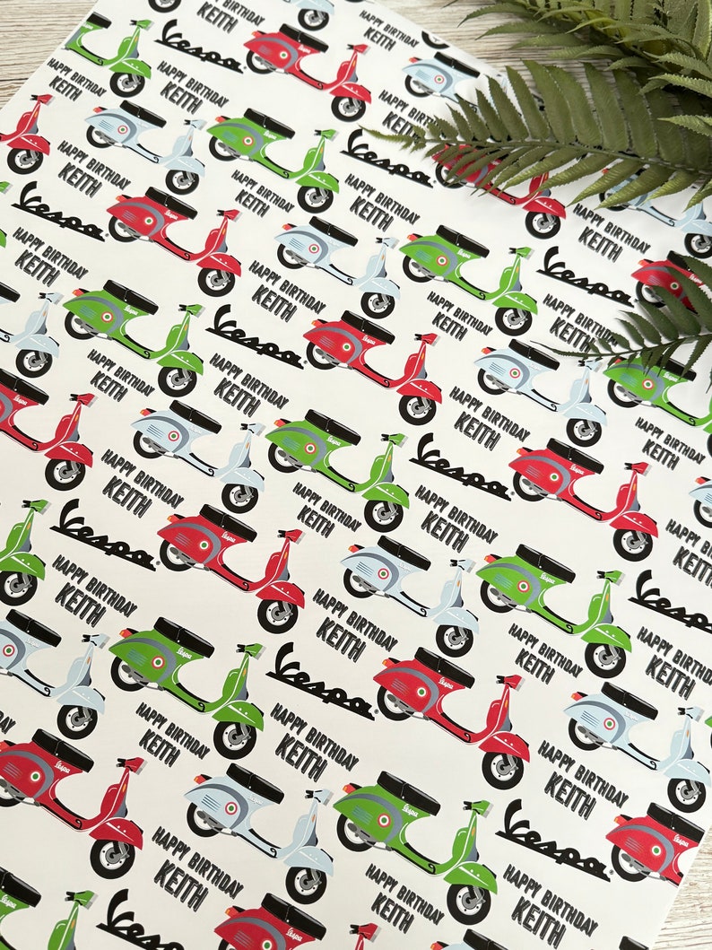 May include: White wrapping paper with a repeating pattern of colorful Vespa scooters. The scooters are red, green, and blue. The text "Happy Birthday Keith" is repeated throughout the pattern.