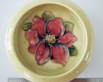 May include: A small, round, ceramic bowl with a pale yellow glaze. The bowl features a hand-painted design of a red flower with green leaves.