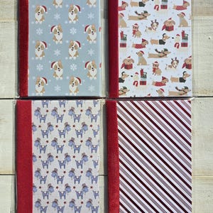May include: Four rectangular notebooks with red velvet-textured spines. The top left features corgis in Santa hats on light blue. The top right shows dachshunds with gifts on white. The bottom left has blue donkeys on white. The bottom right has red stripes.