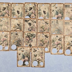 May include: A collection of vintage-style tags with floral and bee illustrations. The tags feature a distressed, aged paper look with faded colors and script. Each tag has a hole at the top and two circular cutouts at the bottom.