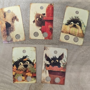 May include: Five rectangular, vintage-style tags with illustrations of cartoon dogs. Each tag features a different dog, with varying colors and poses. The tags have a distressed look with a hole at the top and two at the bottom.