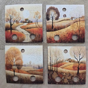 May include: Four square cards with a watercolor landscape scene featuring trees, a winding road, and a small house. The color palette includes shades of orange, brown, and beige, with a circular hole in each corner and one in the center.
