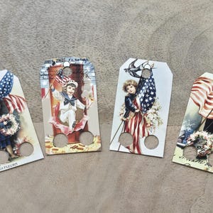 Könnte beinhalten: Vier Geschenk-Anhänger im Vintage-Stil mit patriotischen Themen. Jeder Anhänger zeigt ein Kind mit einer amerikanischen Flagge oder patriotischen Bildern. Die Anhänger haben oben ein Loch zum Aufhängen und unten zwei kleinere Löcher. Der Hintergrund ist ein neutrales Beige.