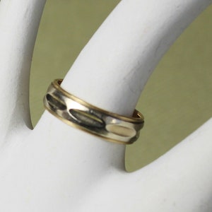 May include: A gold and silver patterned wedding band. The band has a textured design with alternating gold and silver sections.