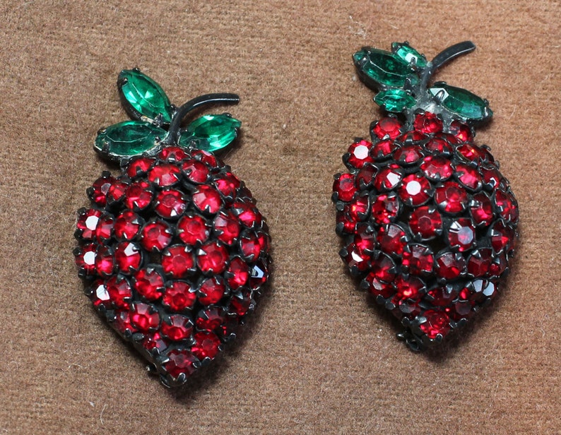 May include: A pair of red and green rhinestone strawberry brooches. The strawberries are made of red rhinestones and have green rhinestone leaves.