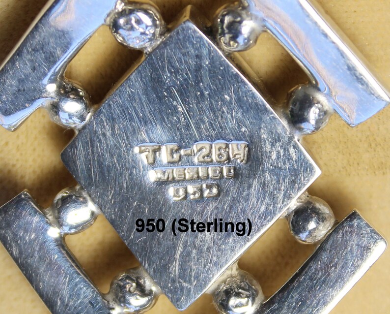 May include: Close-up of a silver pendant with a geometric design. The pendant is marked "TL-264 MEXICO 950" and "950 (Sterling)".