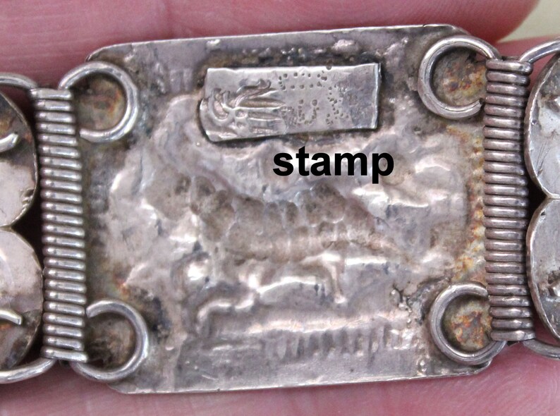 May include: Silver bracelet with a textured design and a stamp that reads "stamp".