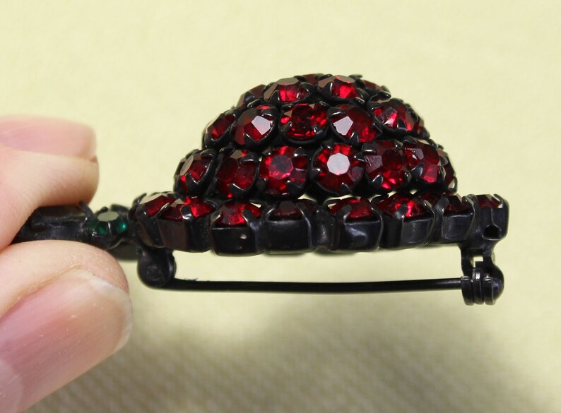 May include: A vintage brooch with a cluster of red rhinestones set in a black metal base. The brooch has a pin and catch closure.