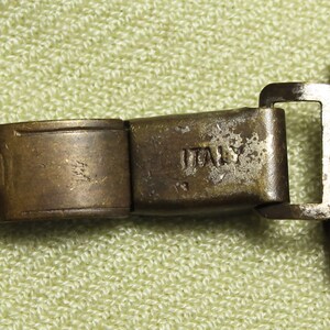May include: Close-up of a metal watch band clasp with the word "ITALY" engraved on it.