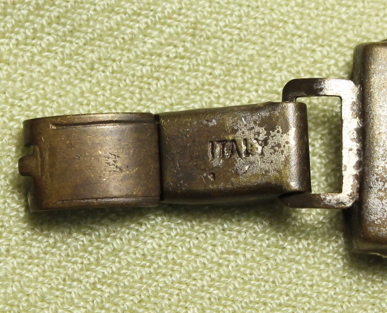 May include: Close-up of a metal watch band clasp with the word "ITALY" engraved on it.