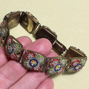 May include: A vintage bracelet made of metal with a floral mosaic design. The mosaic features red, green, blue, and white flowers.