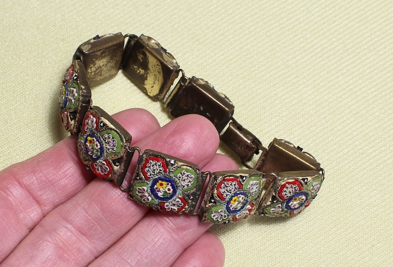 May include: A vintage bracelet made of metal with a floral mosaic design. The mosaic features red, green, blue, and white flowers.