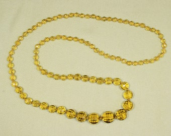 May include: A long strand of amber-colored glass beads, strung together to form a necklace. The beads are faceted and have a slightly rounded shape.