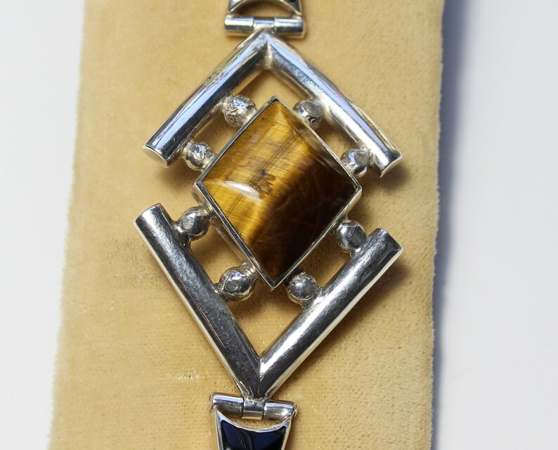May include: A silver bracelet with a geometric design featuring a large, square-shaped tiger's eye gemstone.