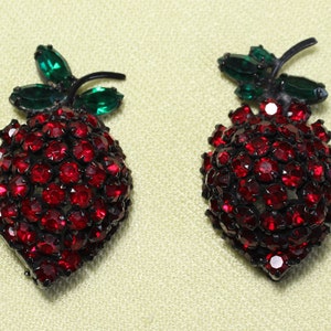 May include: A pair of red rhinestone strawberry brooches with green rhinestone leaves.