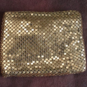 Könnte beinhalten: Eine goldene Clutch aus Mesh mit Kettenglied-Design. Die Clutch besteht aus kleinen, ineinandergreifenden Metallkreisen.