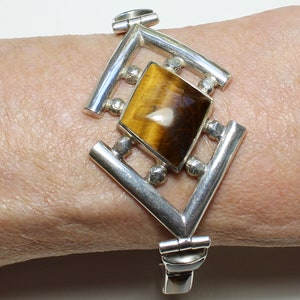 May include: A silver bracelet with a geometric design featuring a large, rectangular tiger's eye gemstone.